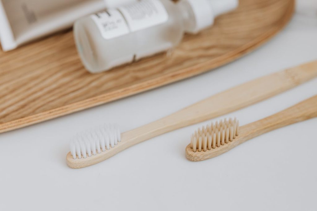 Close-up of two wooden toothbrushes on a white surface with skincare products in a wellness setup.